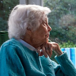 elderly woman looking through window in house